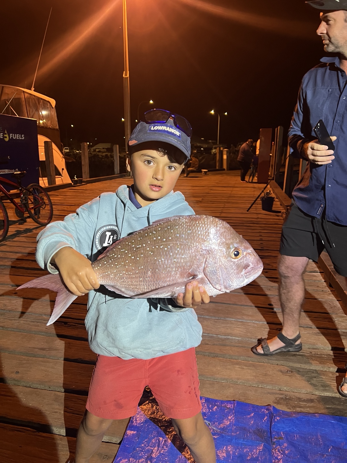 Child holding a fish on a jetty at night